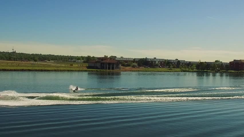 A man skiing in green sea water linked with a boat in the summer with green coast in a distance