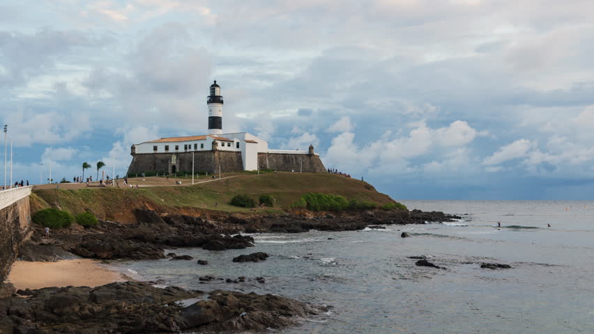 Day to night timelapse of the historic Farol da Barra, the oldest lighthouse in operation on the coast of Brazil and the Americas, in Salvador, Bahia, Brazil, zooming out. 