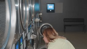 High angle view of young woman with laundry basket walking away from industrial washer, door open, stainless machines in row, laundromat interior, routine workflow, cleaning operation in progress - Powered by Shutterstock - Get 15% off with code: PIKWIZARD15
