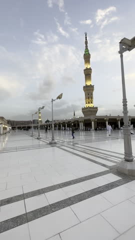 A serene golden-hour view of Al-Masjid an-Nabawi in Madinah, capturing its glowing minarets, tranquil courtyard, and a few walking pilgrims, with worshippers in peaceful reflection.