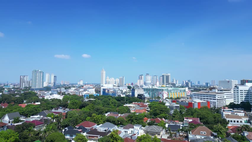 Jakarta City Skyline Rises Above a Dense Tropical Residential Neighborhood and Lush Green Canopy Under Clear Blue Sky