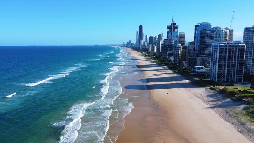 Aerial footage of Surfers Paradise and Broadbeach coastline in Gold Coast, Queensland, Australia. High-rise buildings casting long shadows along the beach with turquoise waves.