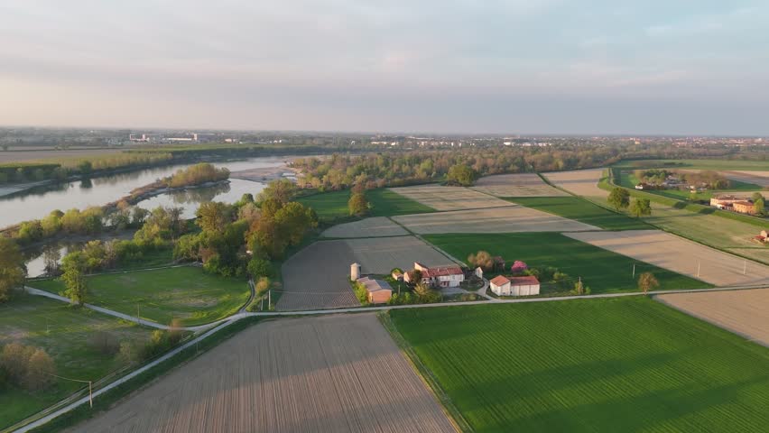 Po River flowing between Lombardy and Piacenza province, Italy, with structured agricultural fields, scattered farm buildings, and tree-lined banks typical of the Padana plain’s rural landscape.