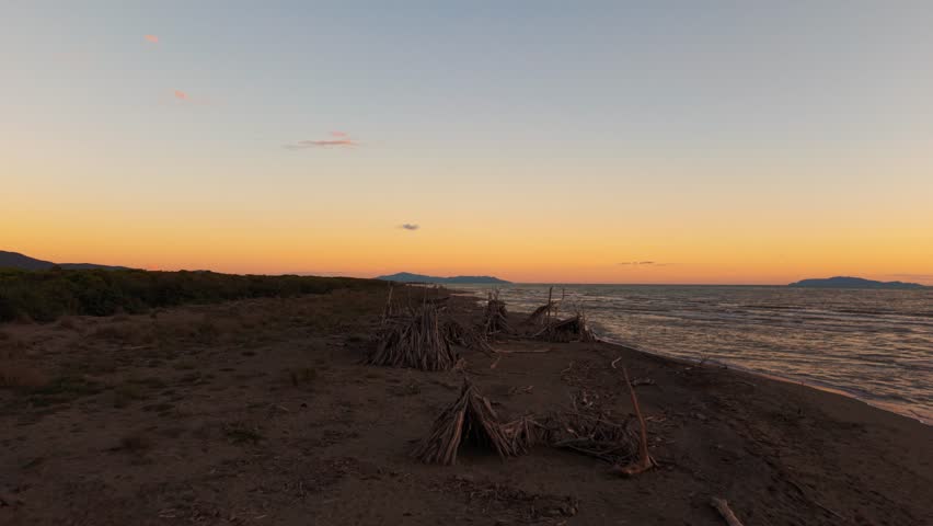Dramatic sky over Tuscany Maremma seaside forested driftwood tipis in evening light. Aerial tilt