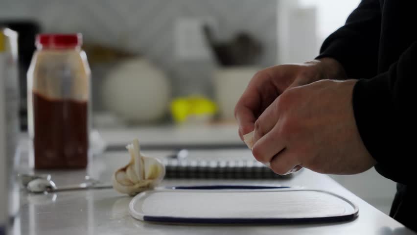 Person with his hands peels off garlic ingredient for Beef Qebapa in home kitchen setting.