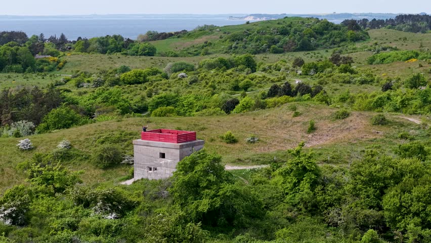 Aerial view of an old German World War II bunker with a red roof, surrounded by overgrown grass and coastal greenery