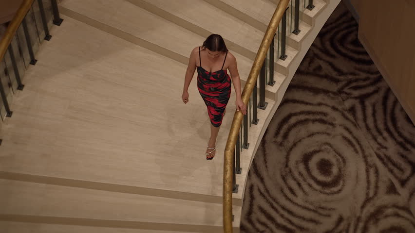 an asian performer in vivid red dress elegantly moves down grand spiral staircase amidst dramatic
