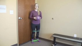 A Caucasian female trainer explaining a Workout exercise using Elastic Bands and resist-A-ball in a room with bench next to her - Powered by Shutterstock - Get 15% off with code: PIKWIZARD15