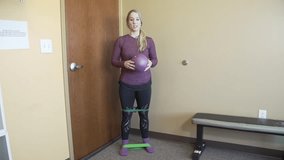 A Caucasian female trainer explaining a Workout exercise using Elastic Bands and resist-A-ball in a room with bench next to her - Powered by Shutterstock - Get 15% off with code: PIKWIZARD15
