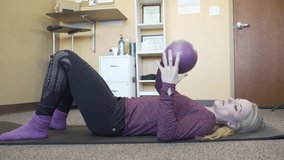 A Caucasian female trainer explaining a workout exercise by lying on yoga mat using resist-A-ball between her legs - Powered by Shutterstock - Get 15% off with code: PIKWIZARD15