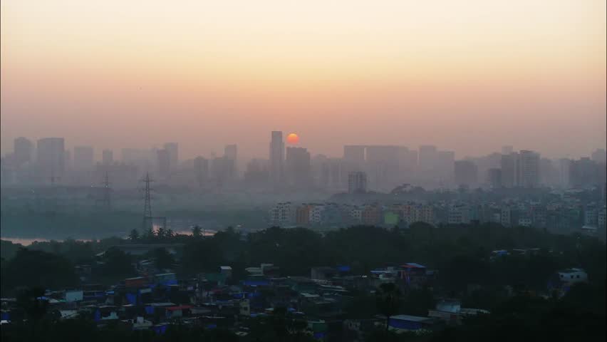 A beautiful time lapse of the sun rising behind an urban landscape of skyscrapers, turning the skies in different hues of orange, with clouds passing over a congested slum locality, Mumbai city, India