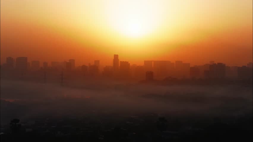 A beautiful time lapse of the sun rising behind an urban landscape of skyscrapers, turning the skies in different hues of orange, with clouds passing over a congested slum locality, Mumbai city, India