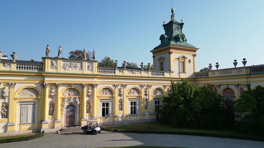 Drone footage of Wilanów Palace in Warsaw with baroque architecture, decorative facade, gardens and scenic morning sunlight highlighting historic royal landmark.