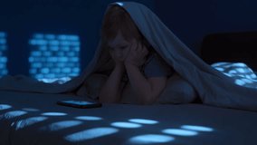 little bored boy in bed at night hiding under blanket, staring at glowing smartphone screen. Digital addiction, excessive screen time, and late-night gadget overuse. - Powered by Shutterstock - Get 15% off with code: PIKWIZARD15