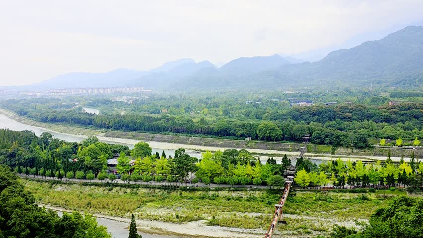A scenic view of a winding river surrounded by lush green mountains under a cloudy sky in Dujiangyan, Sichuan, China.