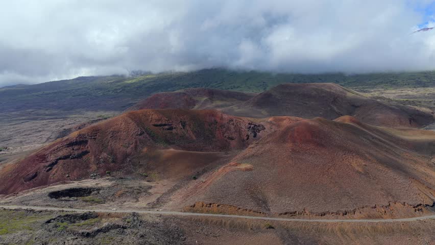 View of Maui’s red volcanic cinder cones and rugged terrain beneath swirling clouds on the road to Hana . Perfect for travel videos, geology content, nature documentaries, and cinematic landscapes.