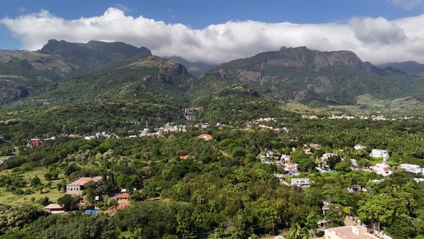 A mesmerising aerial view of a lush South Indian town, Courtallam, nestled at the foothills of the Western Ghats, surrounded by dense greenery and towering mist-clad mountains.