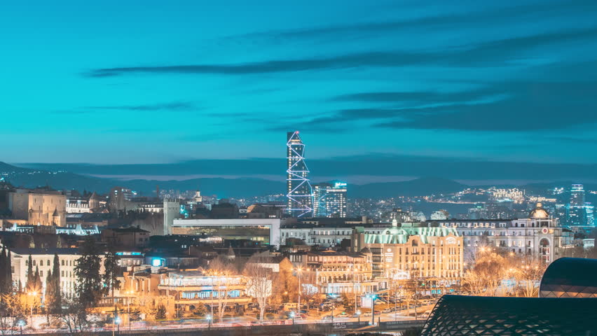 Tbilisi, Georgia. Elevated View Tbilisi Skyline During Sunset Time. 4k Timelapse Radisson Blu Hotel On Background Of Urban Cityscape During Sunset Evening Lights. View Near Tbilisi Music Thaeter And