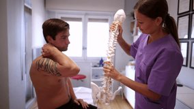 Female doctor showing a tattooed male patient with neck and shoulder pain a model of the human spine, explaining the cause of his discomfort during a consultation in a modern medical clinic - Powered by Shutterstock - Get 15% off with code: PIKWIZARD15