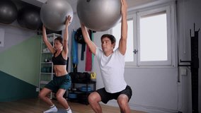 Determined young man and woman performing overhead squats with fitness balls in a gym, focusing on strength, balance, and coordination during an intense couple workout for a healthy lifestyle - Powered by Shutterstock - Get 15% off with code: PIKWIZARD15