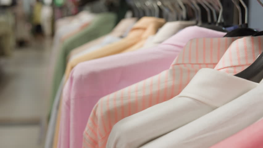 Woman shopper hand choosing shirt from clothing rack in retail store close-up