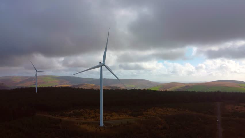 Aerial Reveal of Large Wind Farm Surrounded by Pine Tree Forest with Colorful Blue Sky. Renewable Electric Power Source. Eco-Friendly Energy Generation.