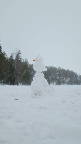 Vertical slowmo shot of child running toward and destroying snowman on snow covered winter field