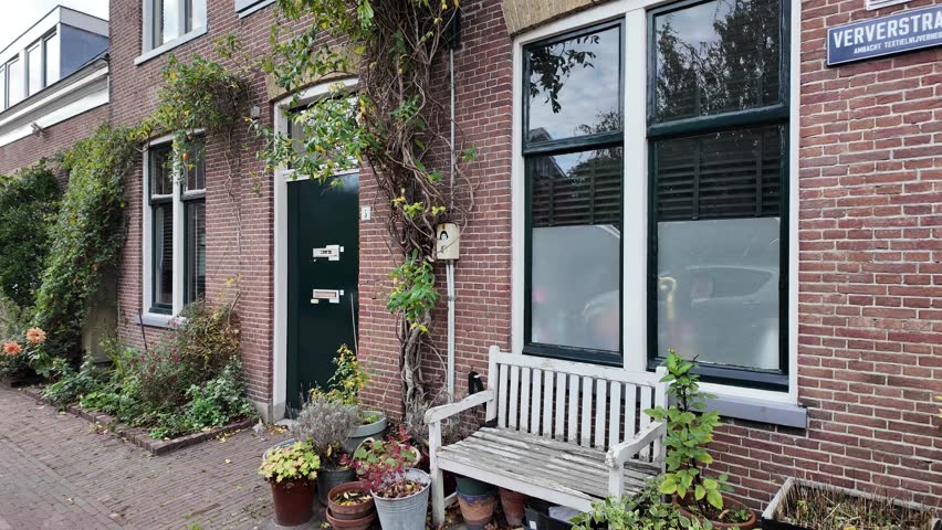 A charming brick house facade is adorned with a vibrant green door, a large window, and lush climbing plants creating a welcoming atmosphere. Leiden, Netherlands