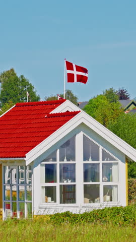 A Danish flag on a flagpole near a traditional house on the seashore at summer