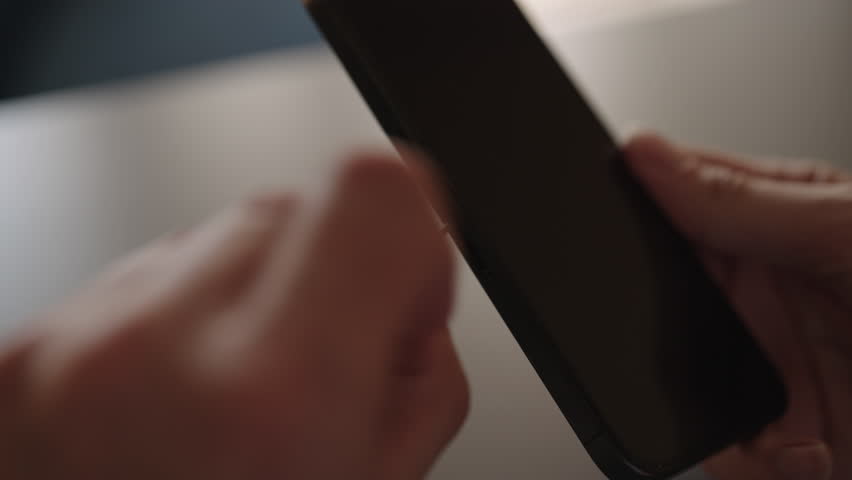 Detail cropped shot of unrecognizable man inserting nano sim card into new smartphone tray sitting on desk, illustrating mobile service transfer, setup, and device upgrade connectivity, slow motion.