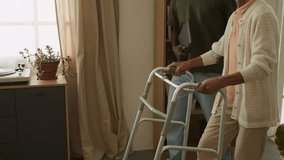 Tilt up shot of white haired senior woman using walker slowly taking steps at home and smiling with caring Black man as social worker assisting, copy space - Powered by Shutterstock - Get 15% off with code: PIKWIZARD15