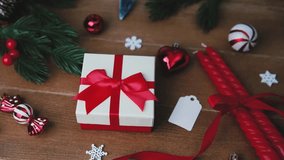 Christmas gift box with red ribbon, ornaments, pine branches, and red candles on wooden table. - Powered by Shutterstock - Get 15% off with code: PIKWIZARD15