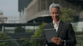 Portrait of grey haired Asian entrepreneur checks data on digital tablet in downtown block. Mature Japanese businessman smiles looking at device screen near office building - Powered by Shutterstock - Get 15% off with code: PIKWIZARD15