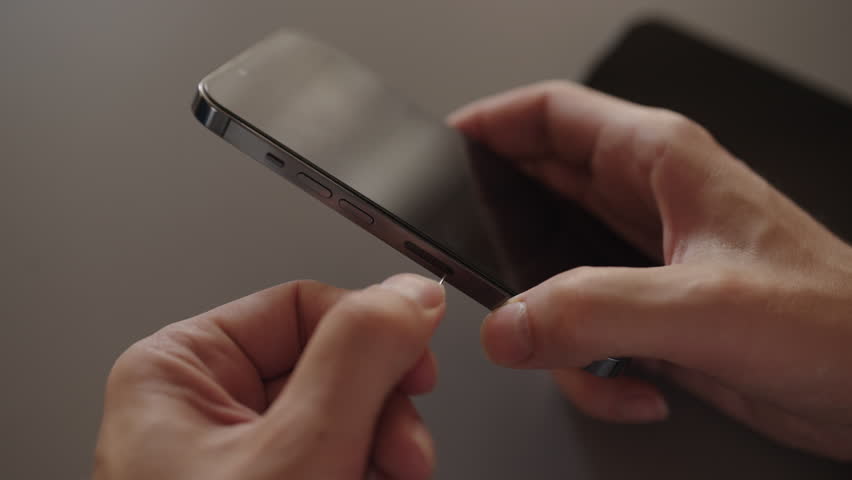 Close-up of male hands holding and inserting nano sim card into new smartphone tray sitting on desk, illustrating mobile service transfer, setup, and device upgrade connectivity, slow motion. - Powered by Shutterstock - Get 15% off with code: PIKWIZARD15