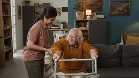 Front view shot of senior man getting up from couch at home using walker with caring young woman assisting, both celebrating with smiles, copy space - Powered by Shutterstock - Get 15% off with code: PIKWIZARD15