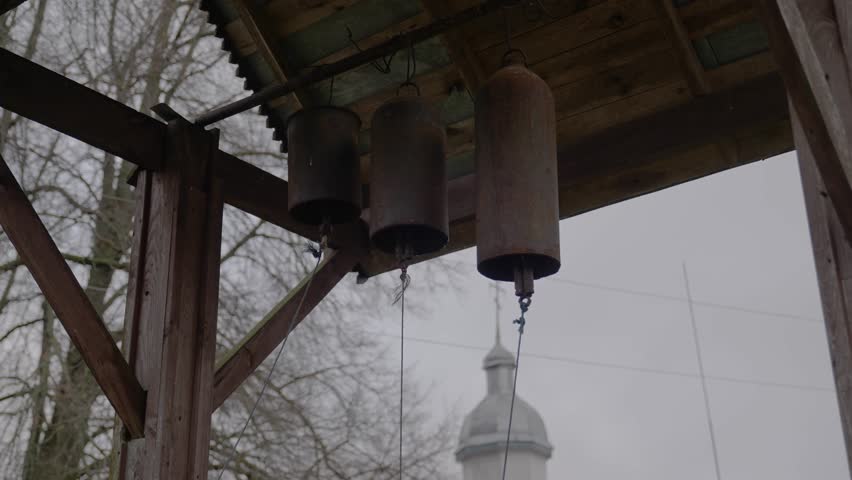 Old rusty church bells against the backdrop of the dome of a village church on a cloudy foggy autumn day.