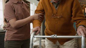 Close up shot of senior man sitting down on couch at home using walker with shaking hands and talking to unrecognizable young woman assisting, copy space - Powered by Shutterstock - Get 15% off with code: PIKWIZARD15