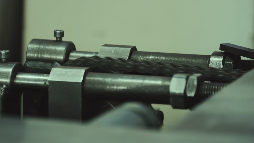 Close up of a mechanical chain drive system in operation, showing the dark metal chain links moving along guides in an industrial manufacturing factory, representing automation and production