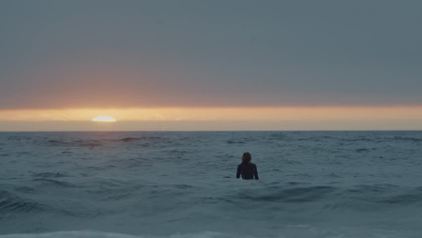 A slow-motion view of a female surfer surfing on foamy waves during sunset