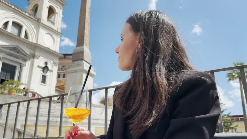 Young fashion woman tourist in casual attire having spritz cocktail with panoramic view of Spanish steps in Rome, slow motion isolated shot