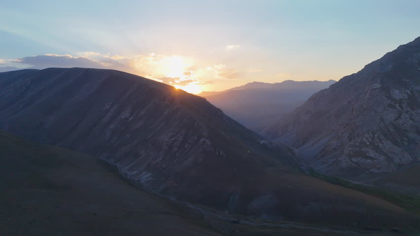 As the sun sets, warm golden light gently illuminates the peaks of the mountains, creating a serene and picturesque scene filled with soft shadows and evening calm.