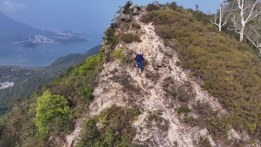 A Caucasian climber riding a rocky mountains with green hills below and water in hong kong