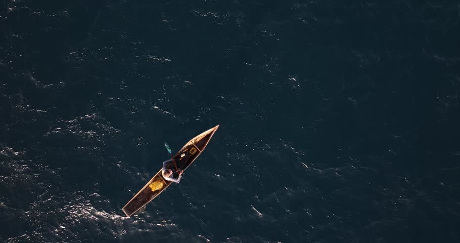 An aerial shot of a man paddling a narrow wooden boat on the coast of Mozambique in Cabo Delgado