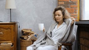 Peaceful woman in pajamas sitting in a comfortable armchair, wrapping herself in a cozy warm blanket and enjoying a hot cup of coffee or tea while relaxing in her loft style apartment - Powered by Shutterstock - Get 15% off with code: PIKWIZARD15