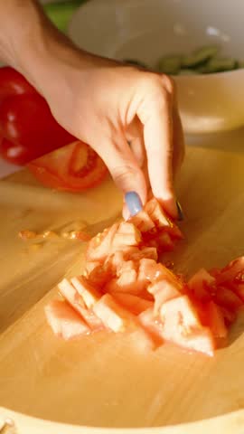 Woman Dicing Red Tomato on a Wooden Cutting Board with Other Vegetables Nearby in Bright Kitchen, side angle, Healthy Eating Concept.