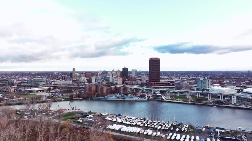 A wide aerial drone view of Buffalo, New York, showcasing the city skyline from the waterfront along the Buffalo River and Canalside district. The image includes the downtown high-rises, historic arch