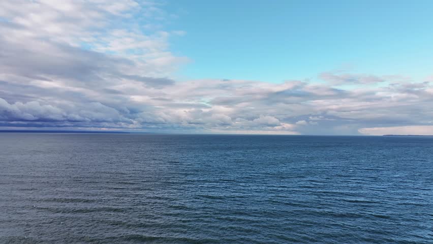 Aerial drone view of the vast waters of Lake Erie near Buffalo, New York. The shot captures gentle waves moving across the deep blue lake under a dramatic sky filled with layered clouds and patches of