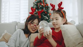 Enjoying a cozy holiday moment by the Christmas tree with family while sharing joy and laughter over a snow globe - Powered by Shutterstock - Get 15% off with code: PIKWIZARD15