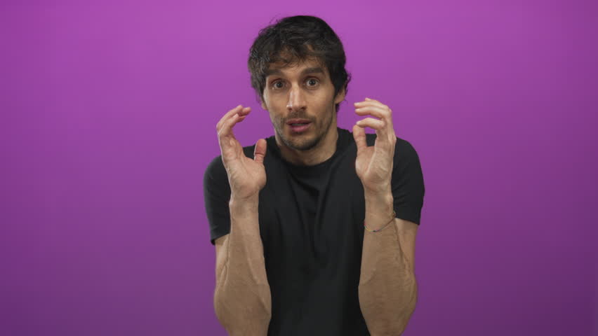 Young man raising hands defensively in studio with purple wall and tense expression and hunched posture; anxiety. - Powered by Shutterstock - Get 15% off with code: PIKWIZARD15