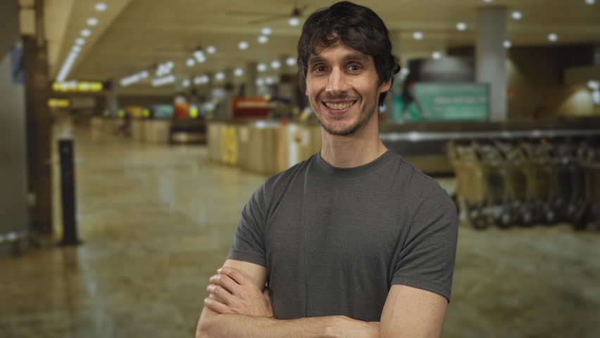 Man crosses arms and turns head with slight smile at airport terminal; quiet confidence.